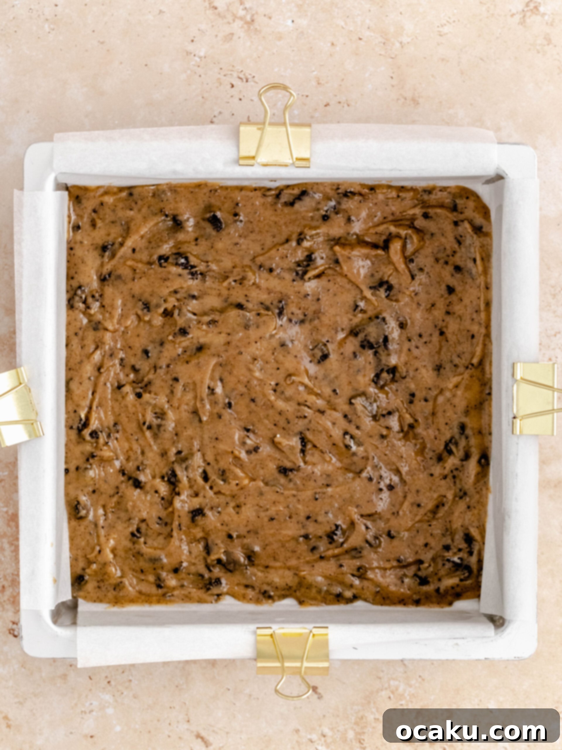 Three-quarters of the Oreo cookie dough spread evenly in a square baking pan.