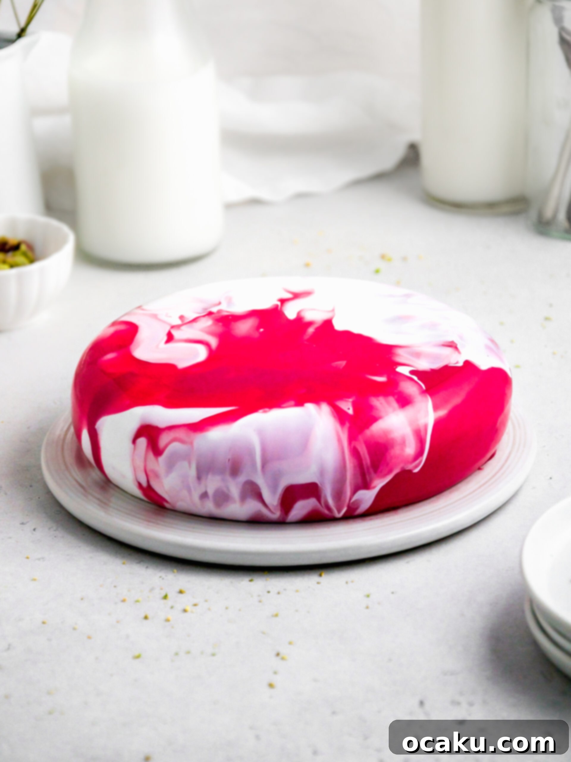 A close-up shot of the stunning multi-colored mirror glaze on the strawberry and pistachio mousse cake, highlighting its glossy, reflective surface.