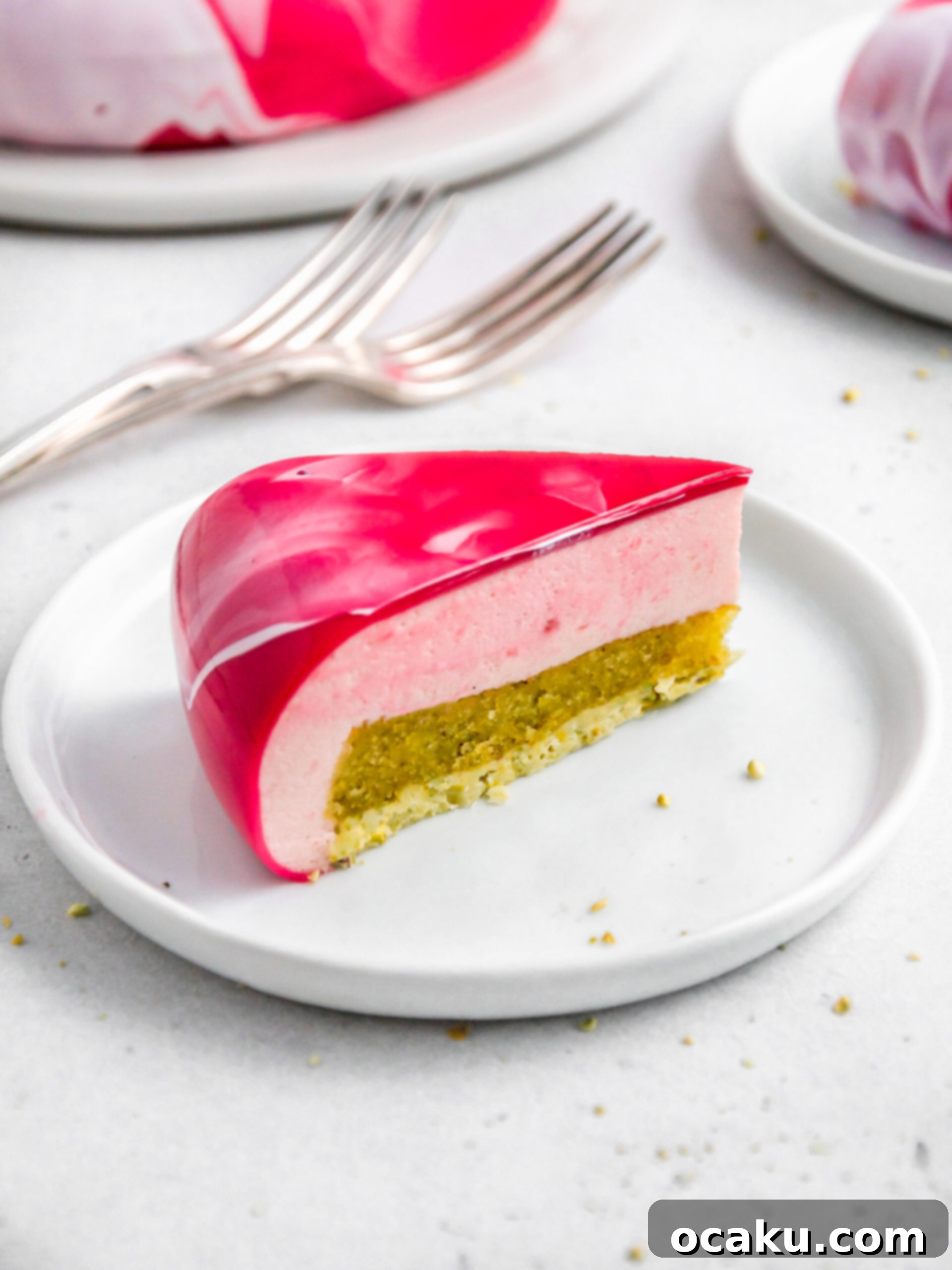 A slice of the strawberry and pistachio mousse cake, showcasing its beautiful layers and mirror glaze, ready to be enjoyed.