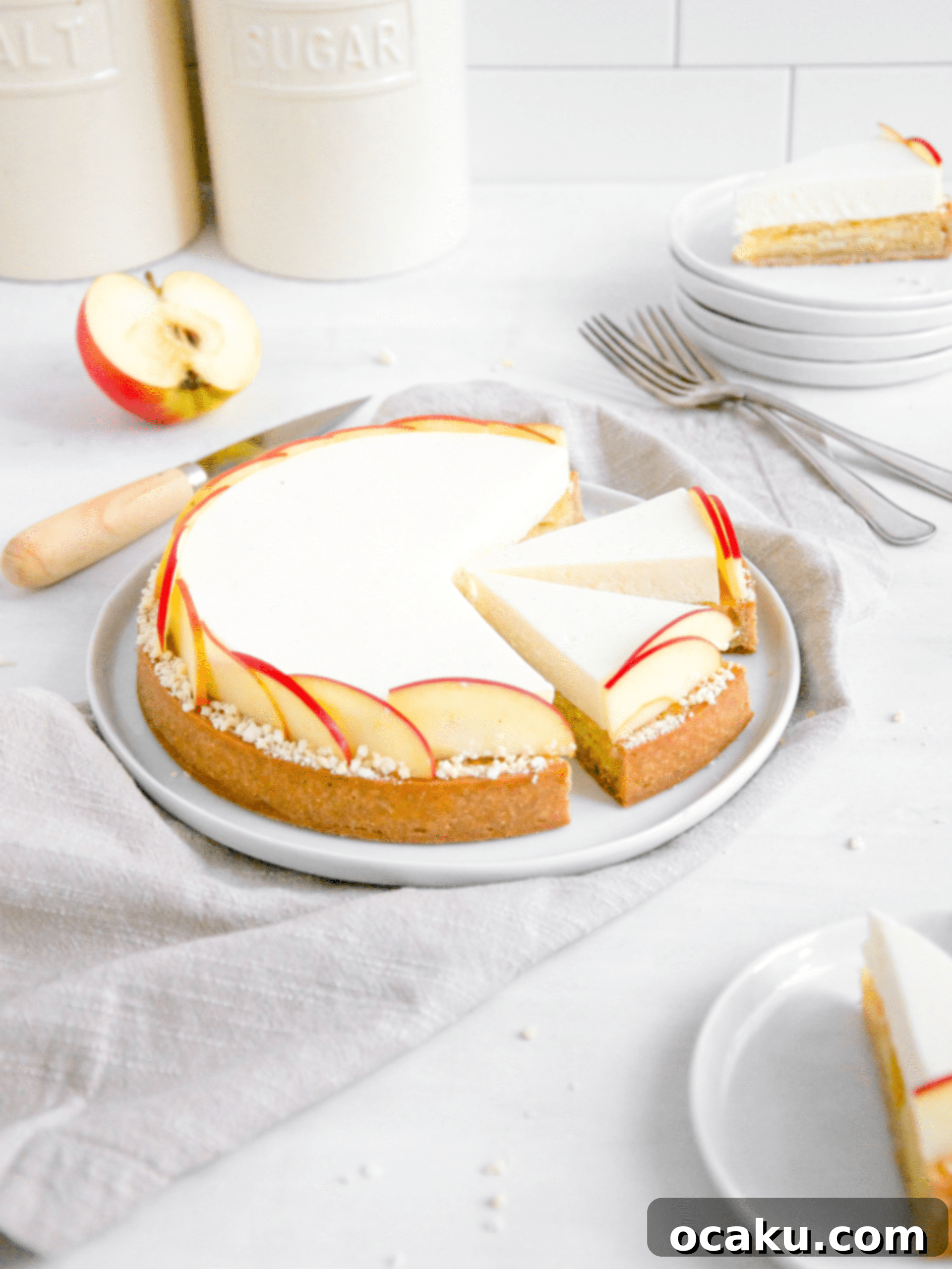 A perfectly sliced apple mousse tart, showcasing layers of golden crust, creamy frangipane, and airy mousse, garnished with fresh apple and white chocolate.