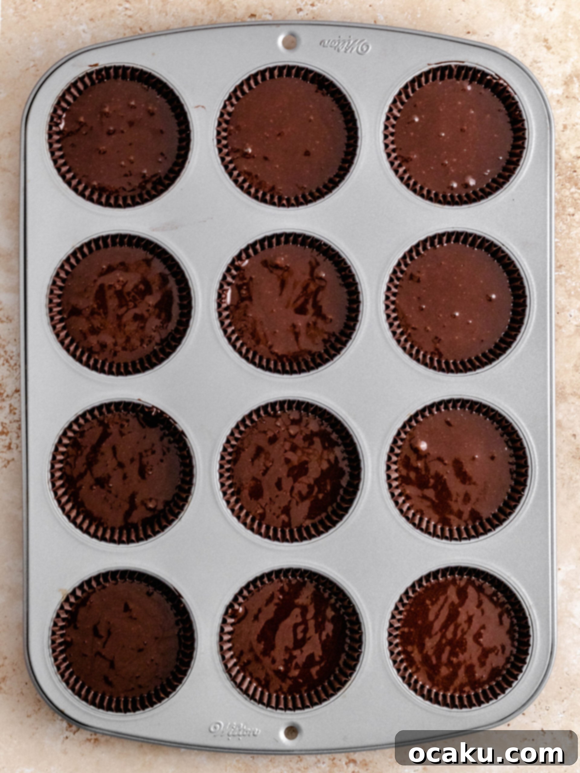 Chocolate cupcake batter being scooped evenly into cupcake liners for baking.