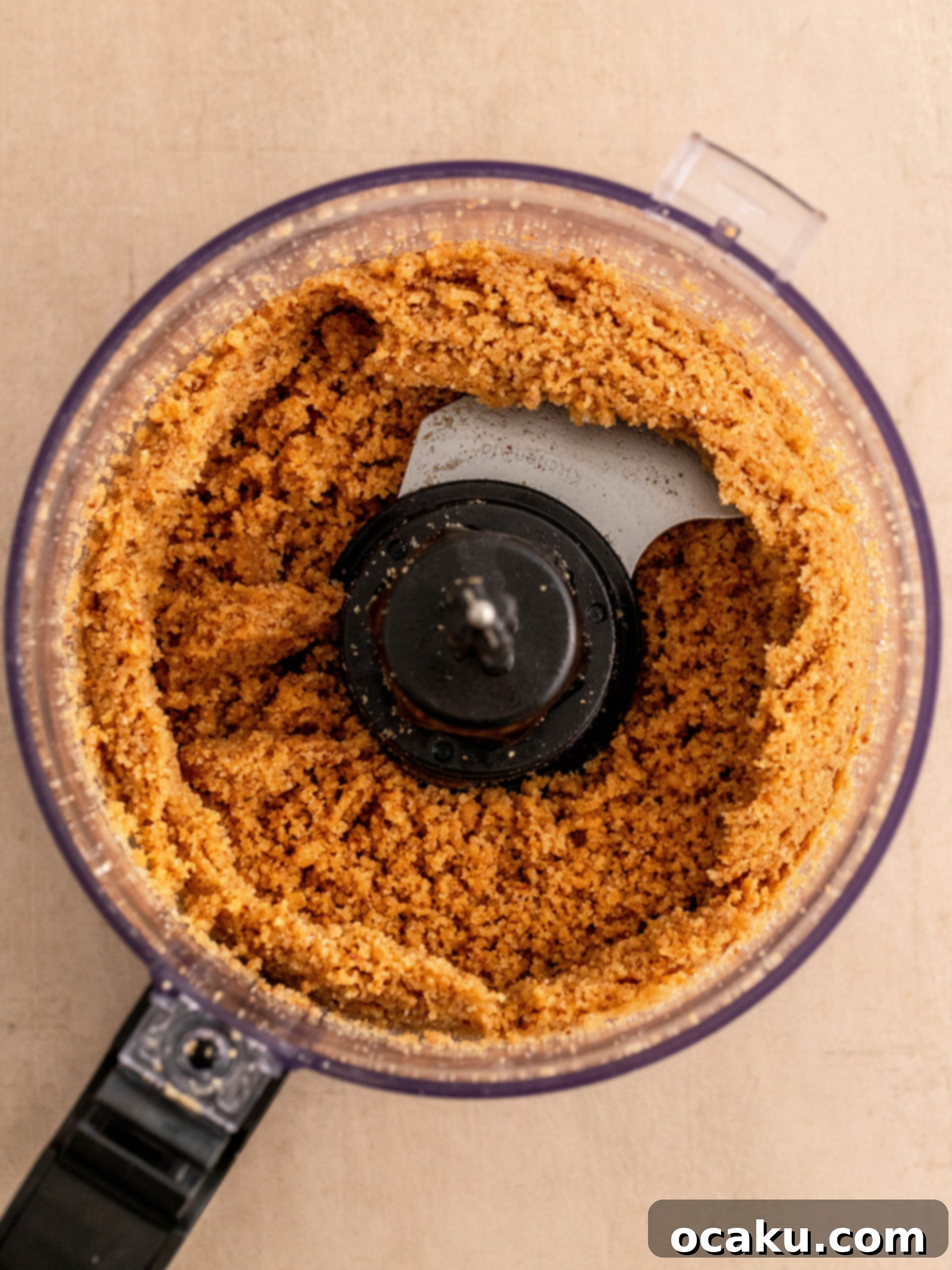 Step-by-step image showing melted butter being added to the blended cookie and pecan mixture.