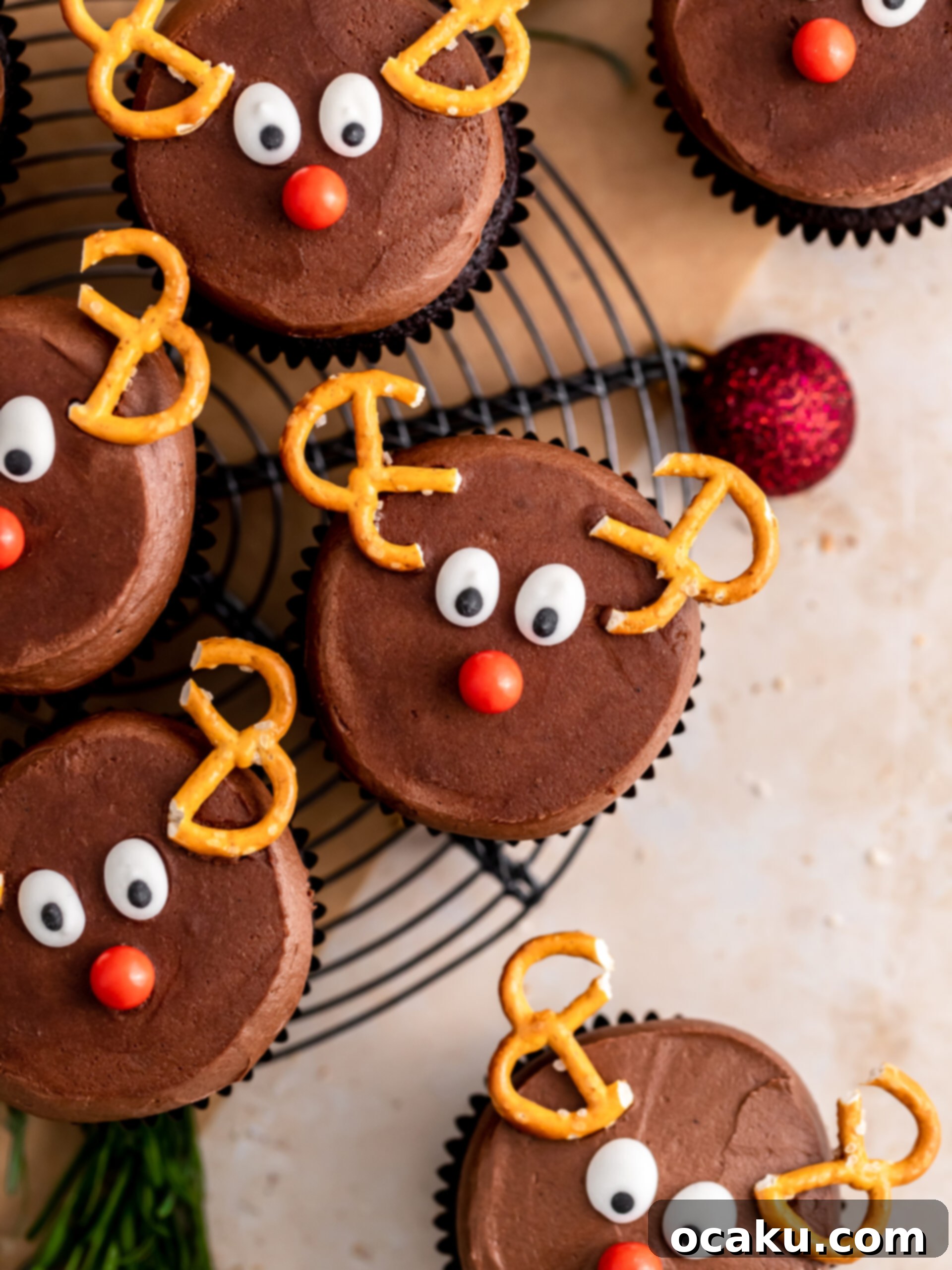 Adorable Reindeer Cupcakes with chocolate frosting, pretzel antlers, candy eyes, and a red sprinkle nose, arranged festively.