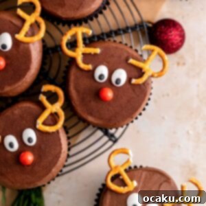Close-up of a festive chocolate reindeer cupcake with pretzel antlers, candy eyes, and a red sprinkle nose.