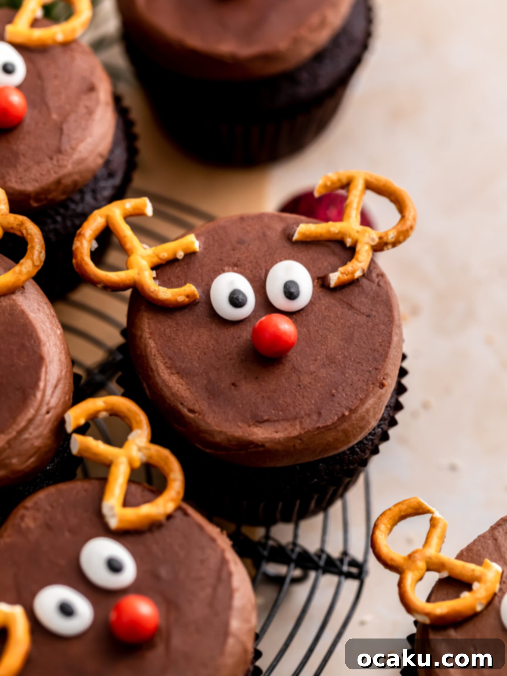 Close-up of a decorated reindeer cupcake, showing the chocolate buttercream, pretzel antlers, candy eyes, and red nose.