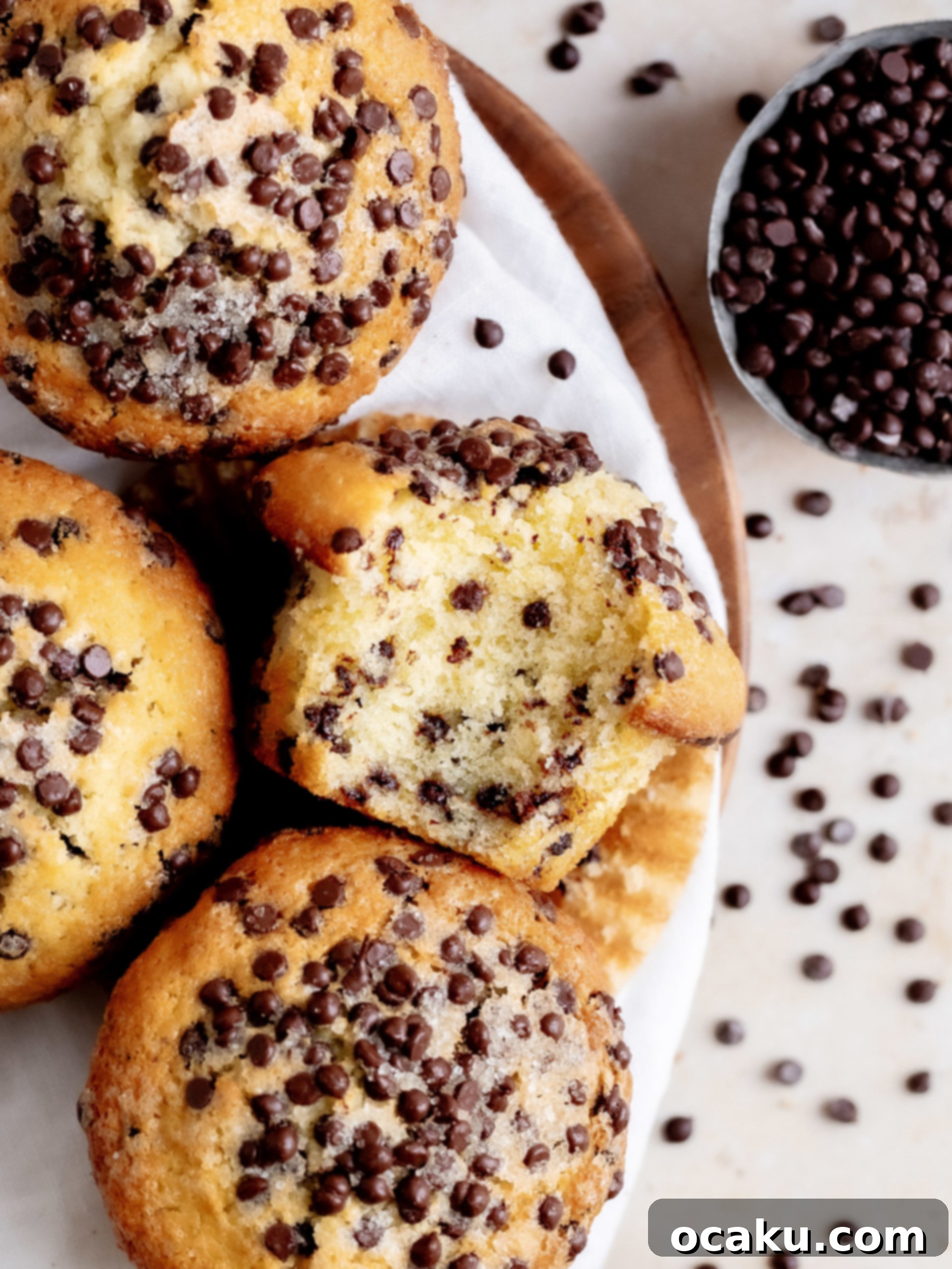 Freshly baked bakery-style chocolate chip muffins with tall, golden tops, studded with melted chocolate chips, resting in a muffin tin.
