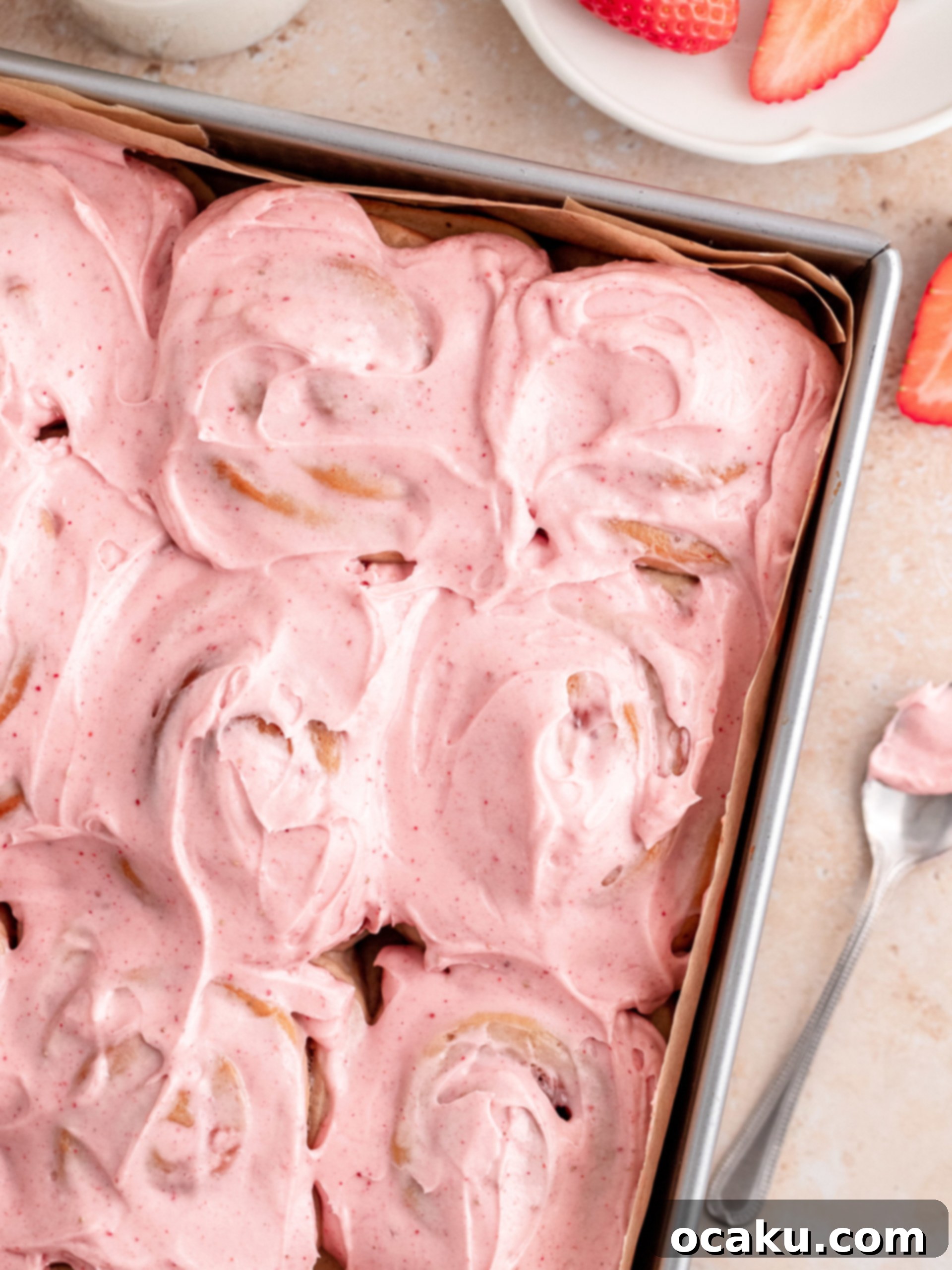 Close-up of baked strawberry rolls in a baking dish, with rich strawberry jam peeking through the swirls.