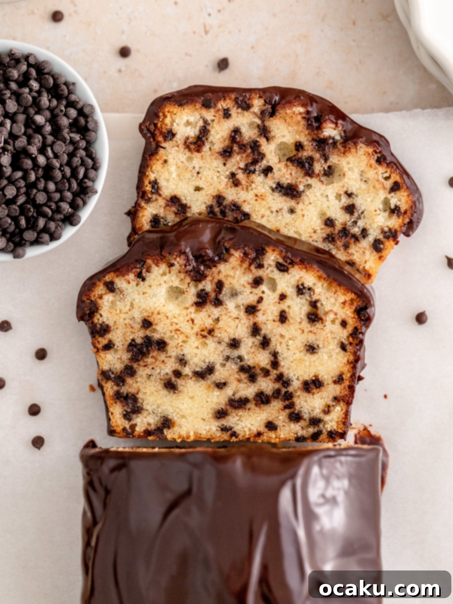A slice of moist chocolate chip loaf cake on a plate, topped with chocolate ganache and chocolate chips.