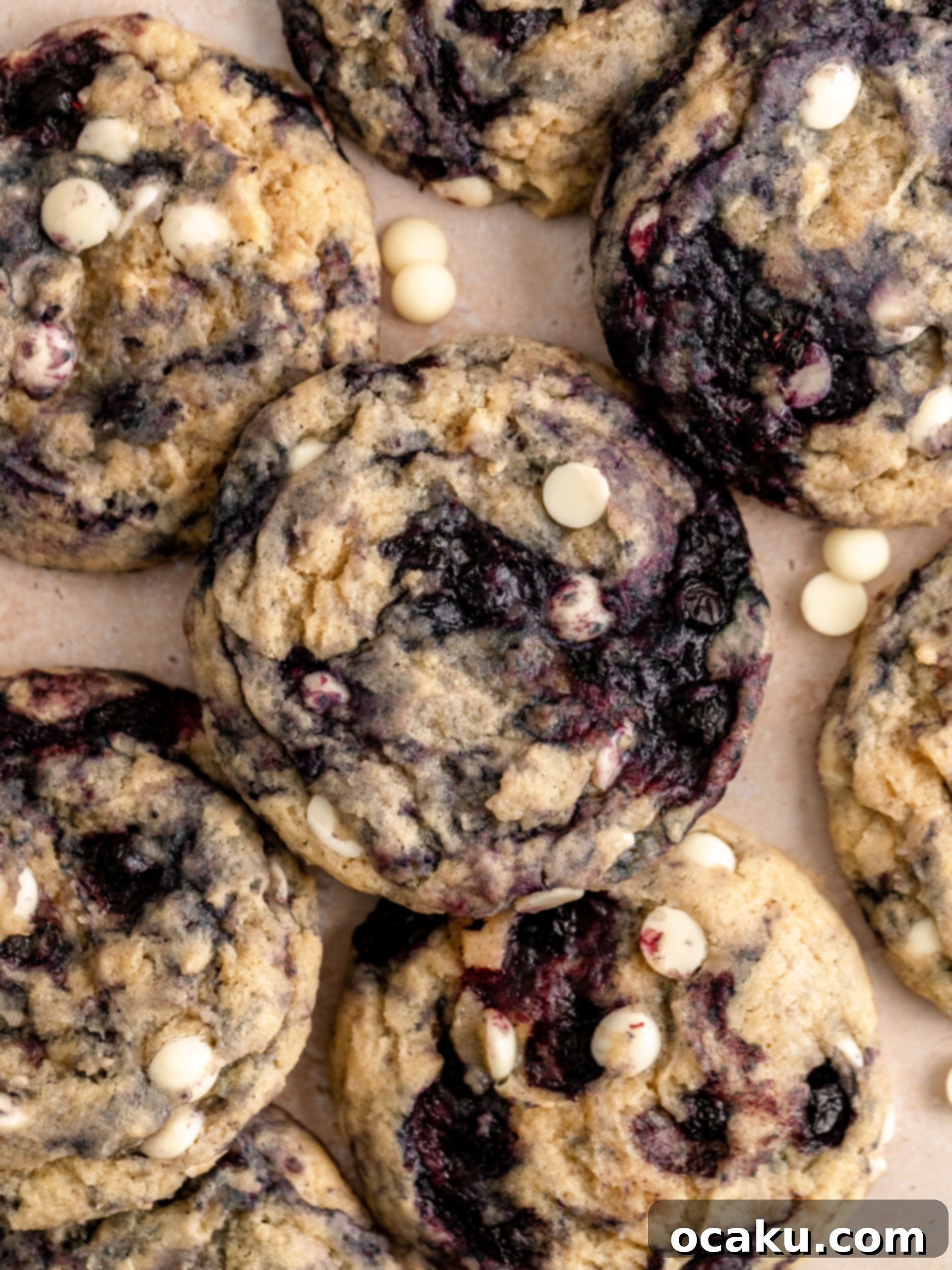 A stack of golden, freshly baked Lemon Blueberry Cookies with visible blueberries and white chocolate on a white surface.