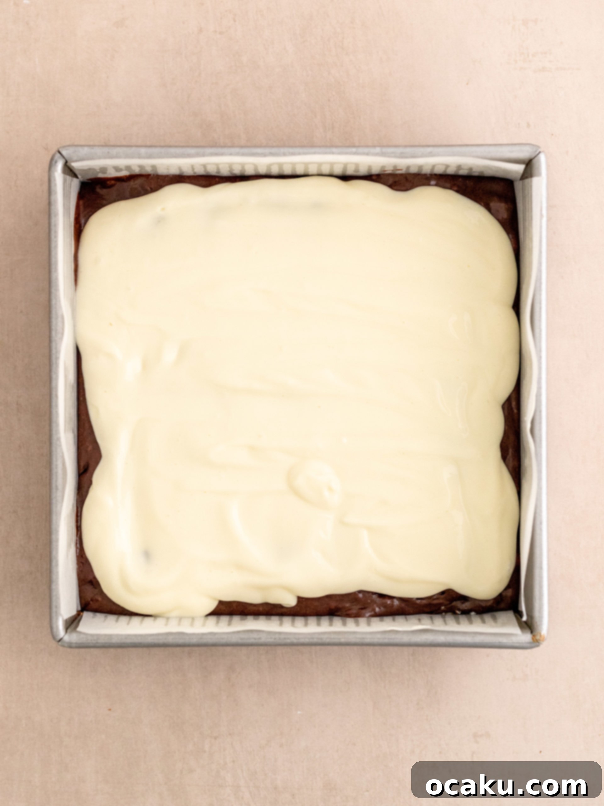 Layering cheesecake batter over the brownie base and dolloping remaining brownie batter on top.