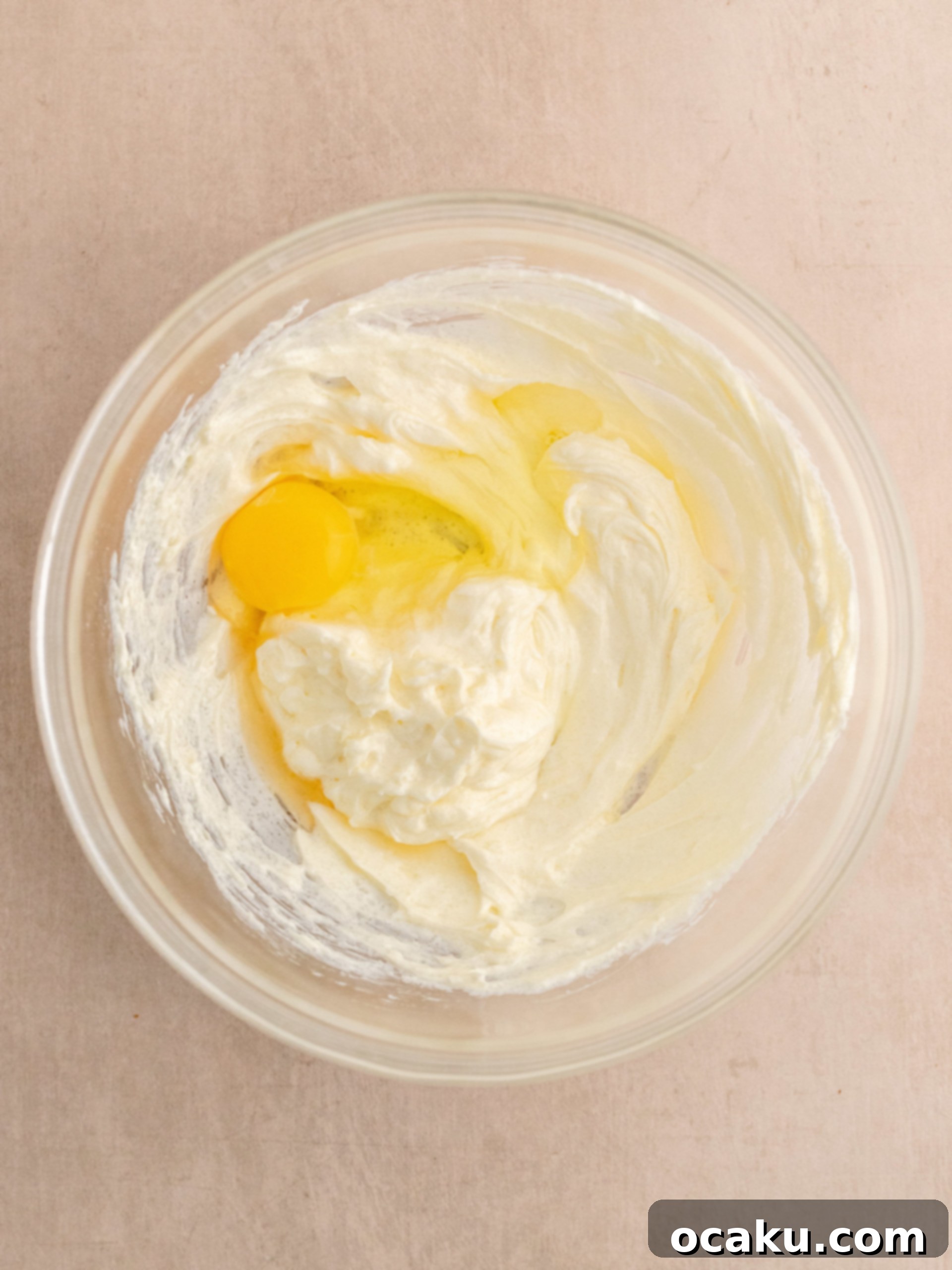 Adding egg and vanilla extract to the cheesecake batter, then whisking until smooth.