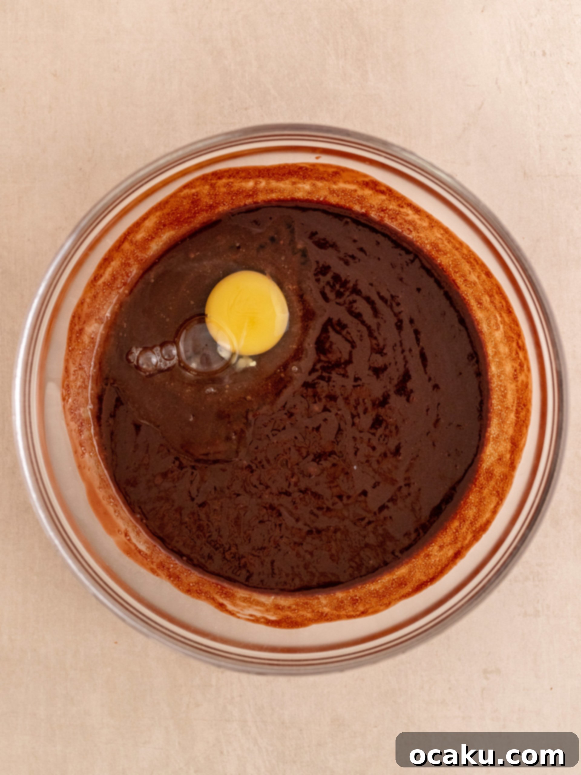 Adding eggs one at a time and whisking vigorously to create the crinkly brownie top.