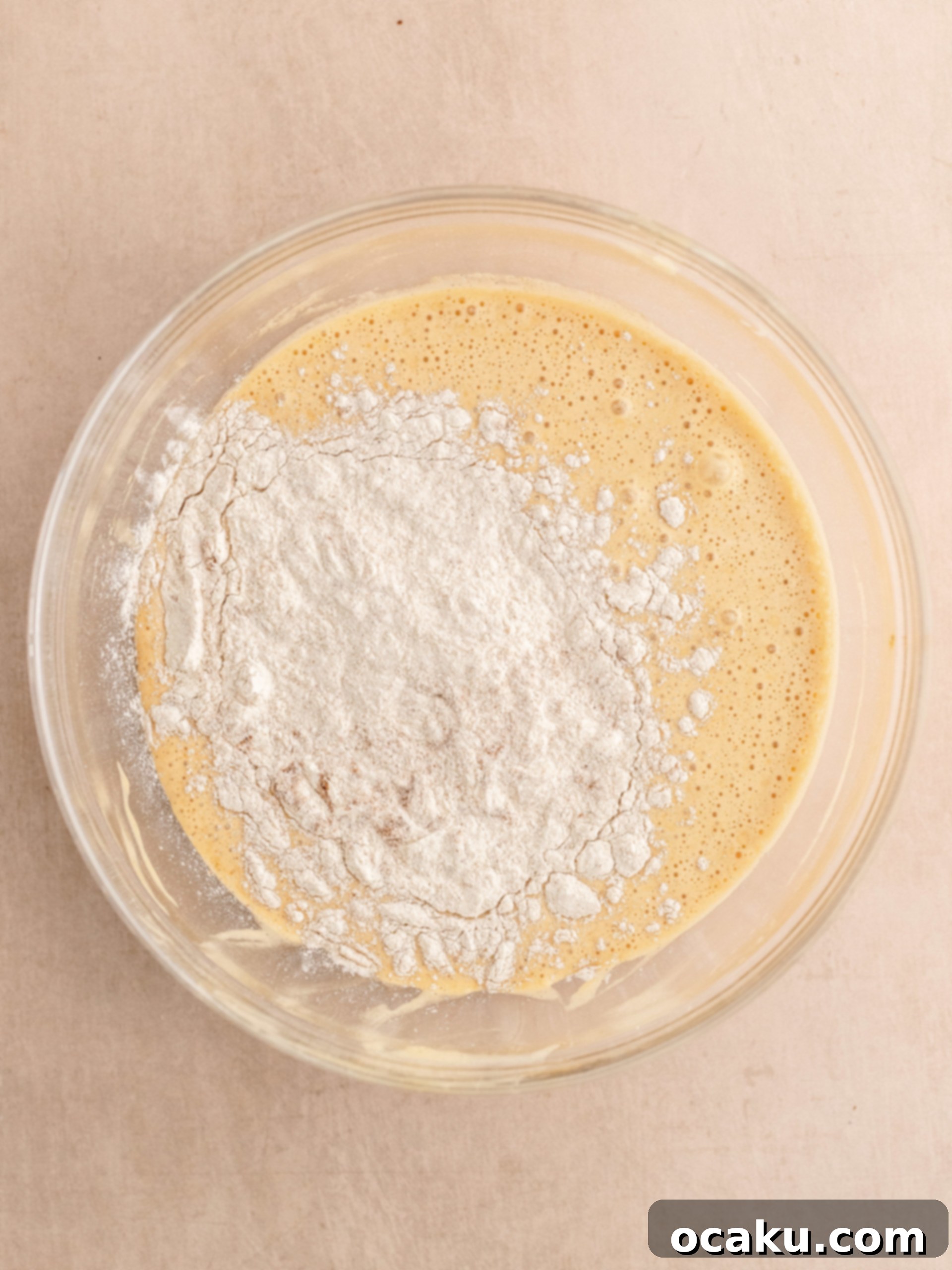 Vegetable oil being slowly poured into the whisked egg and sugar mixture in a stand mixer.
