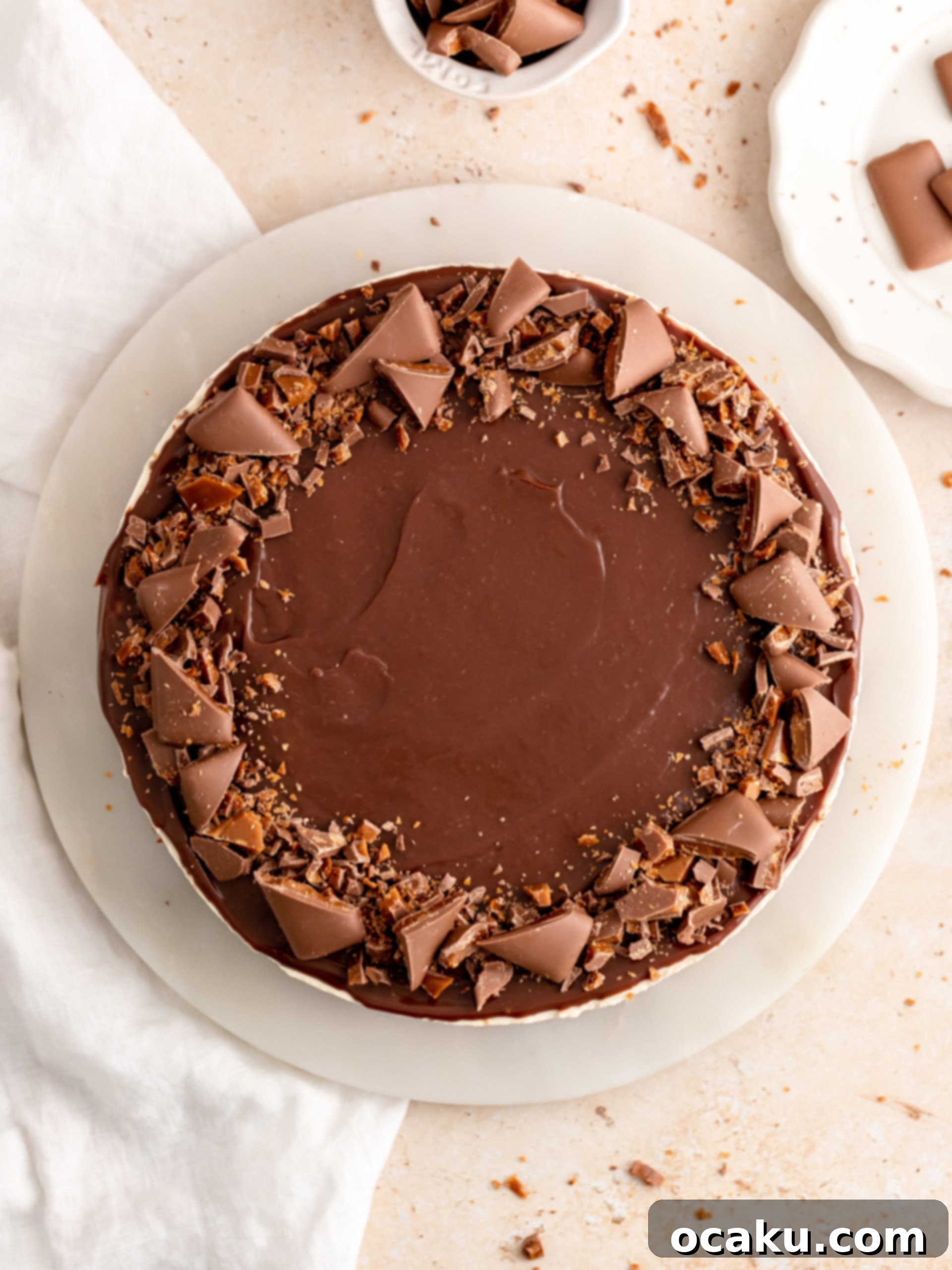Chopped Daim pieces being sprinkled onto the ganache-topped cheesecake.