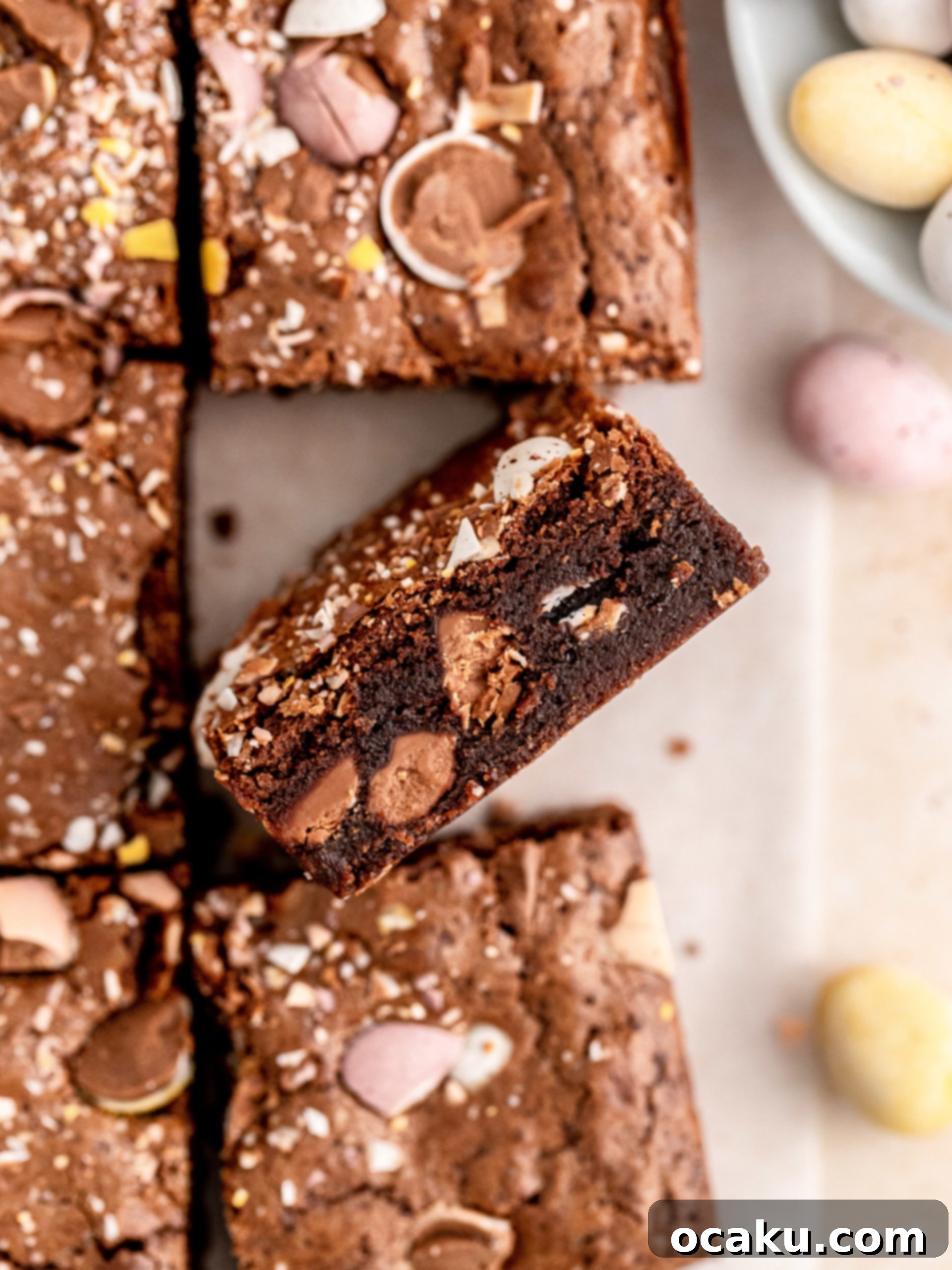 Close-up of freshly baked Mini Egg Brownies, showing the rich, dark chocolate interior studded with colorful Cadbury Mini Eggs, signaling a fudgy texture.