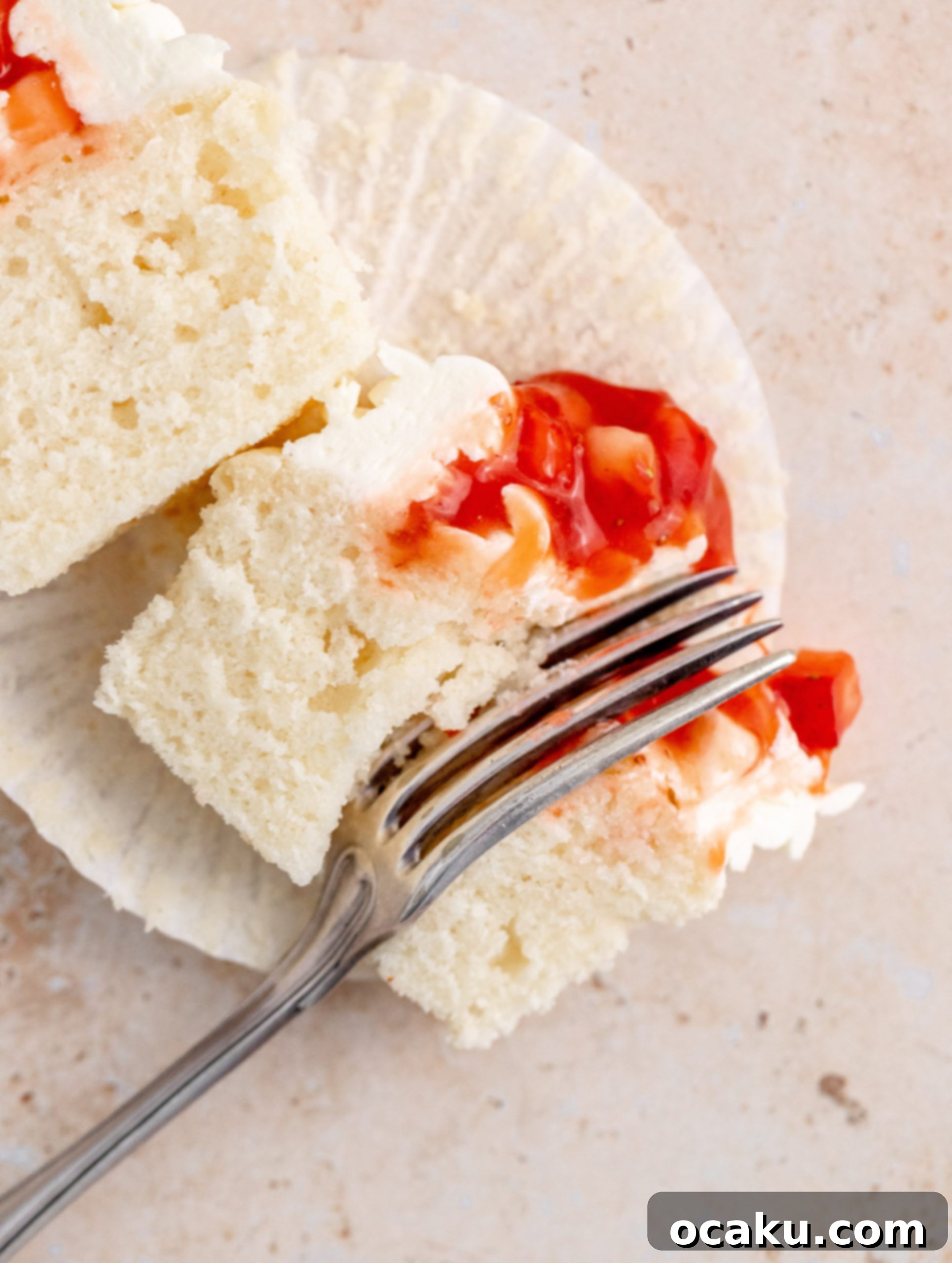 Sweet Strawberry Vanilla Cupcakes 14 A close-up shot of a single strawberry vanilla cupcake with a bite taken out, showing the compote filling.