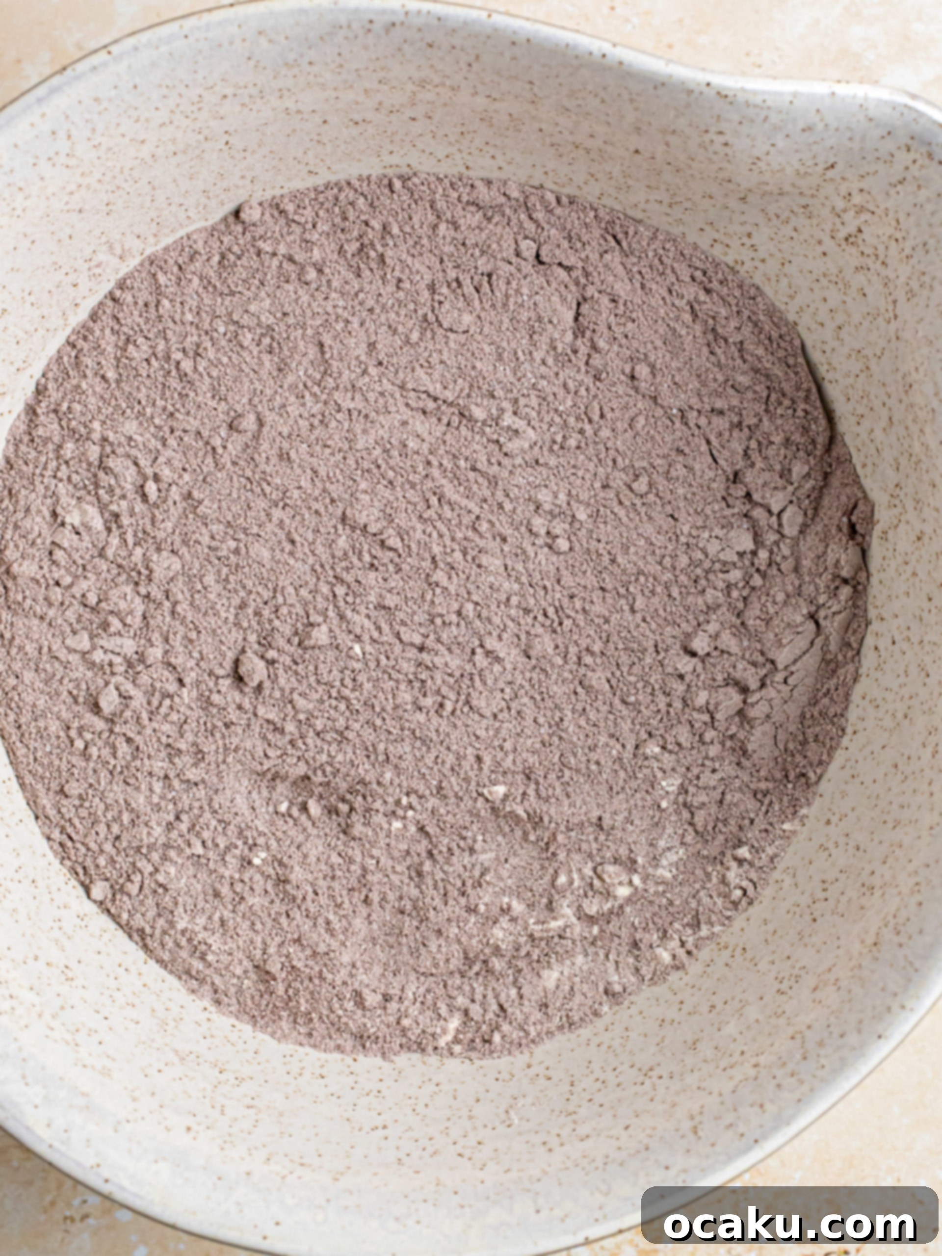 Chocolate cake batter being poured into a round baking pan.