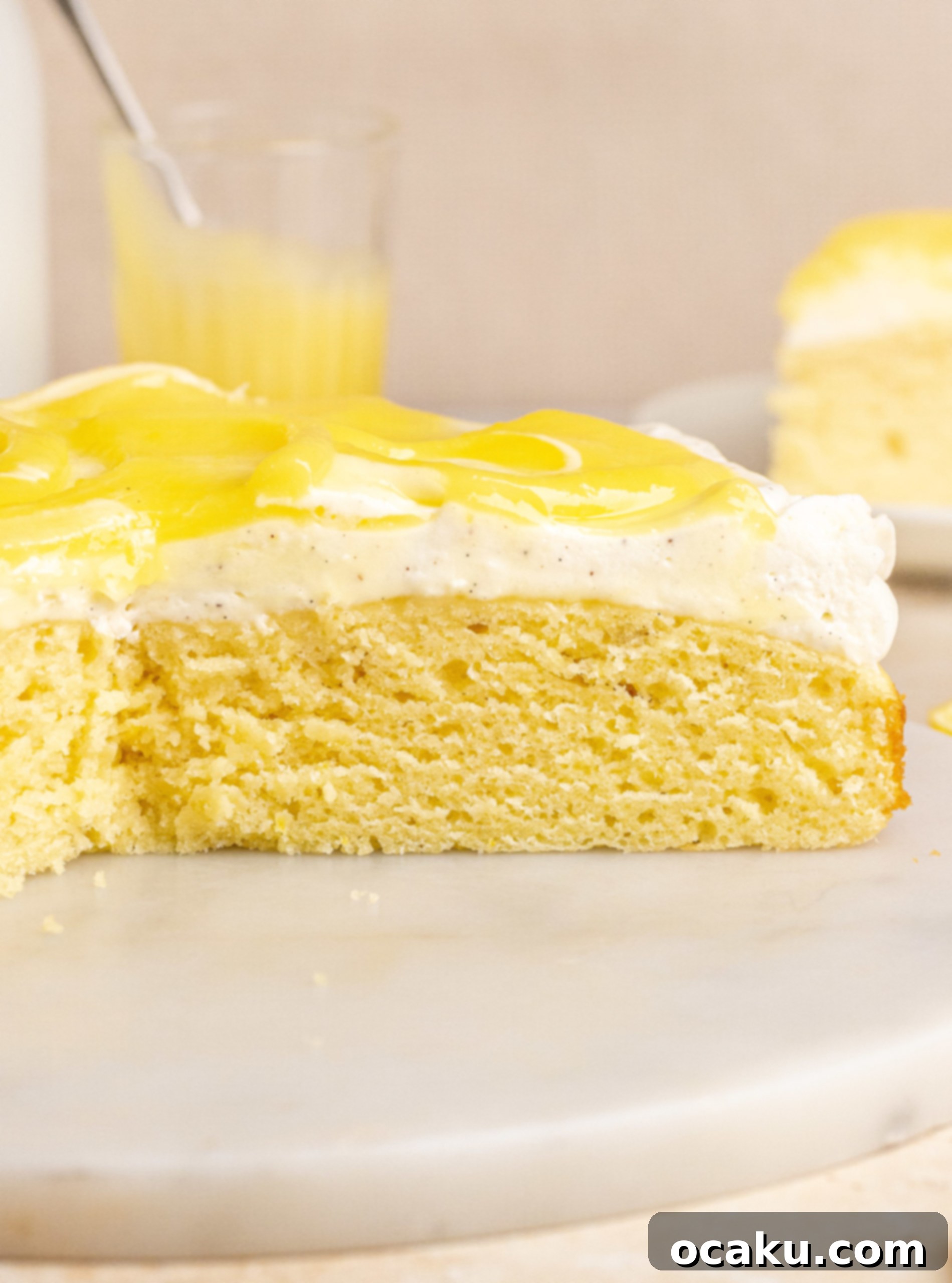 Slice of lemon curd cake on a plate with more of the cake in the background