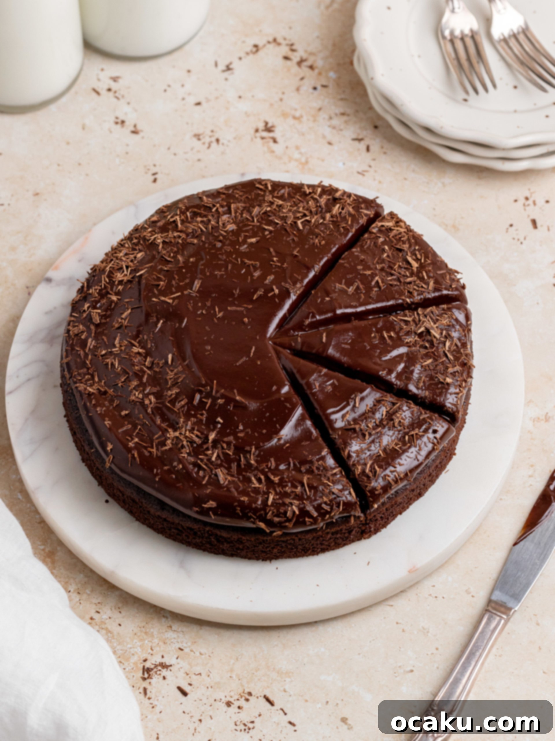 A slice of rich chocolate ganache cake on a white plate, showcasing its moist texture and glossy frosting.