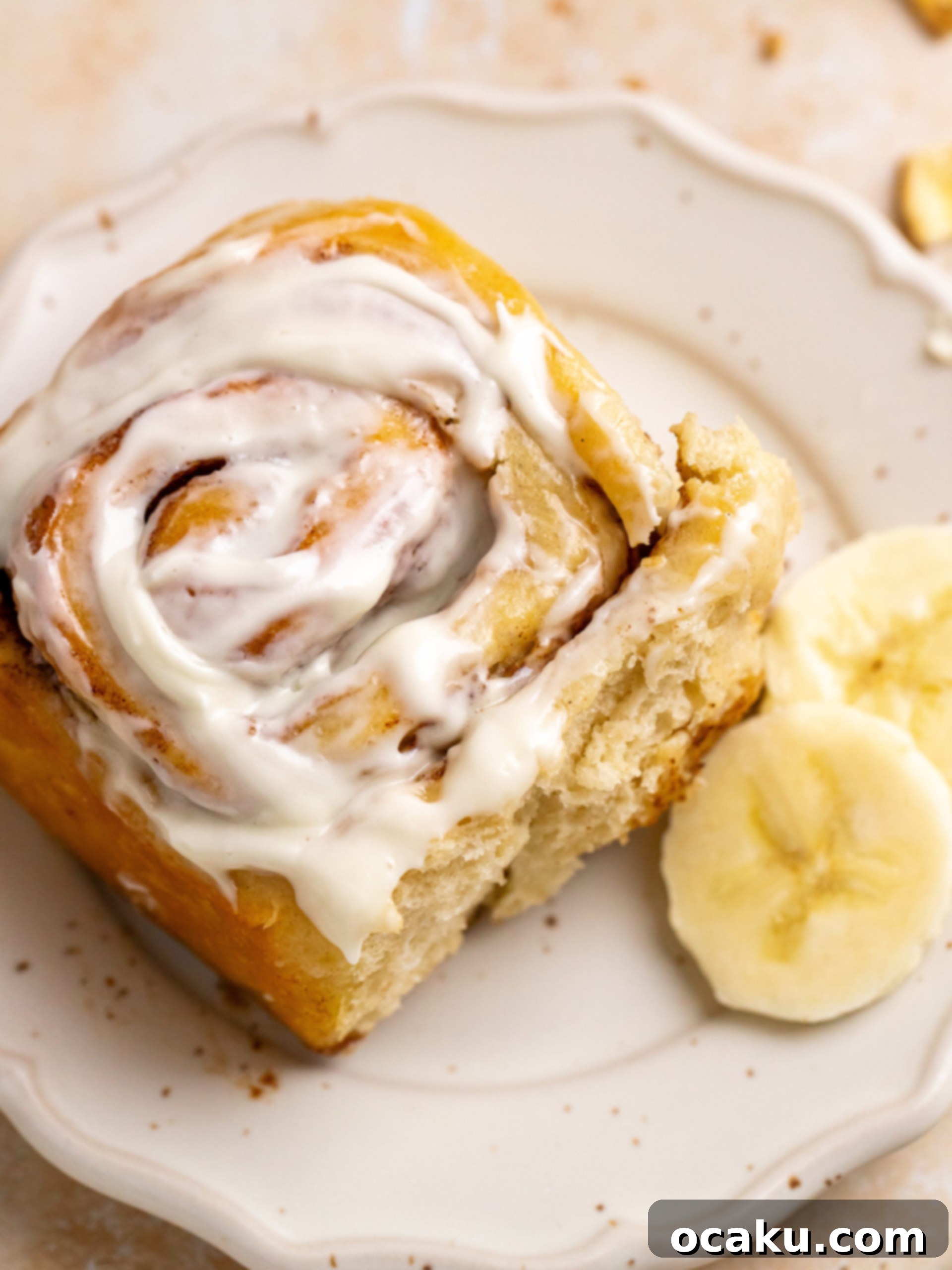 A single banana cinnamon roll with generous cream cheese frosting on a plate.