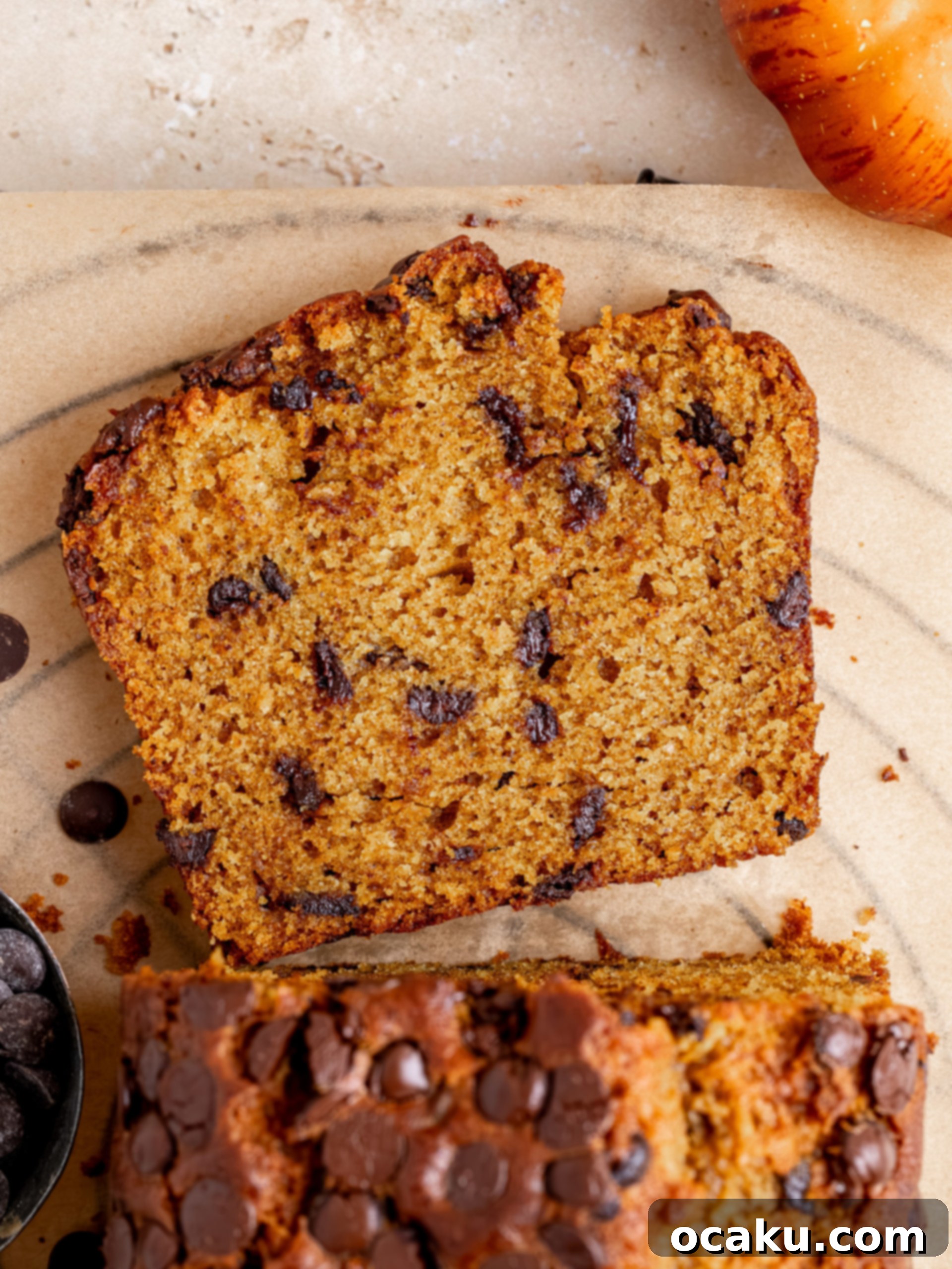 A beautifully baked pumpkin chocolate chip bread loaf on a wooden cutting board, garnished with extra chocolate chips.
