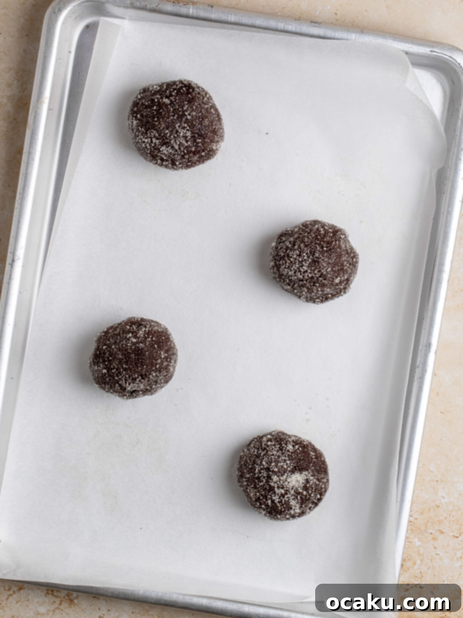 Freshly rolled Nutella Stuffed Cookie dough balls coated in granulated sugar, ready for baking on a parchment-lined tray.