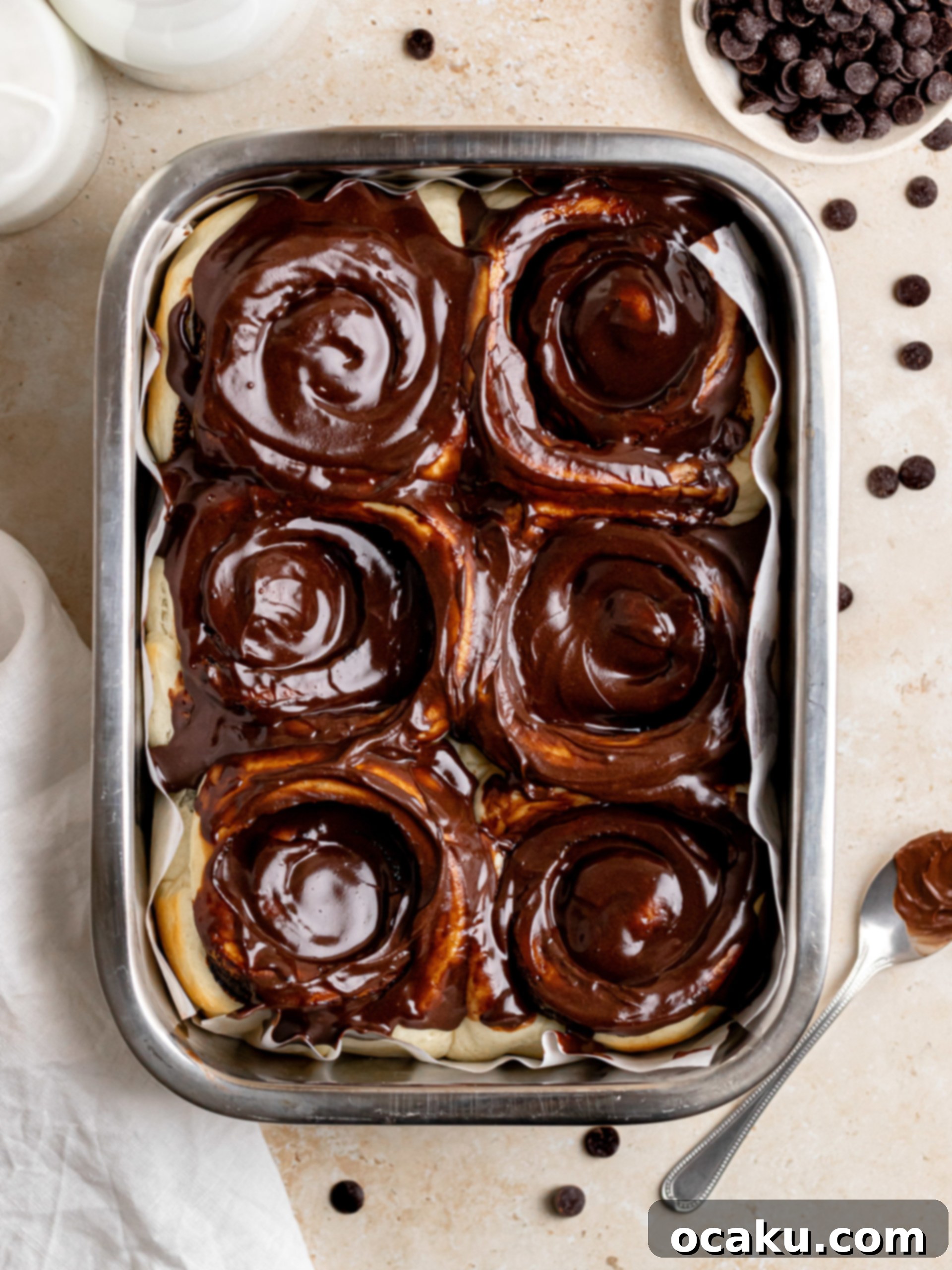 Baked chocolate cinnamon rolls topped with chocolate cream cheese frosting in a baking dish