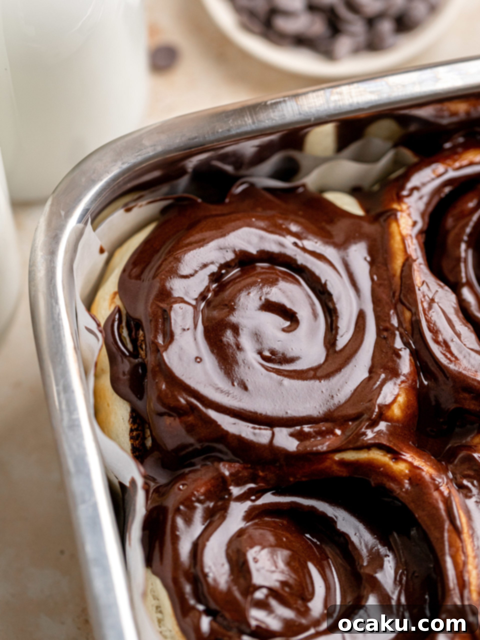 Close-up of a chocolate cinnamon roll with frosting on a plate, ready to eat