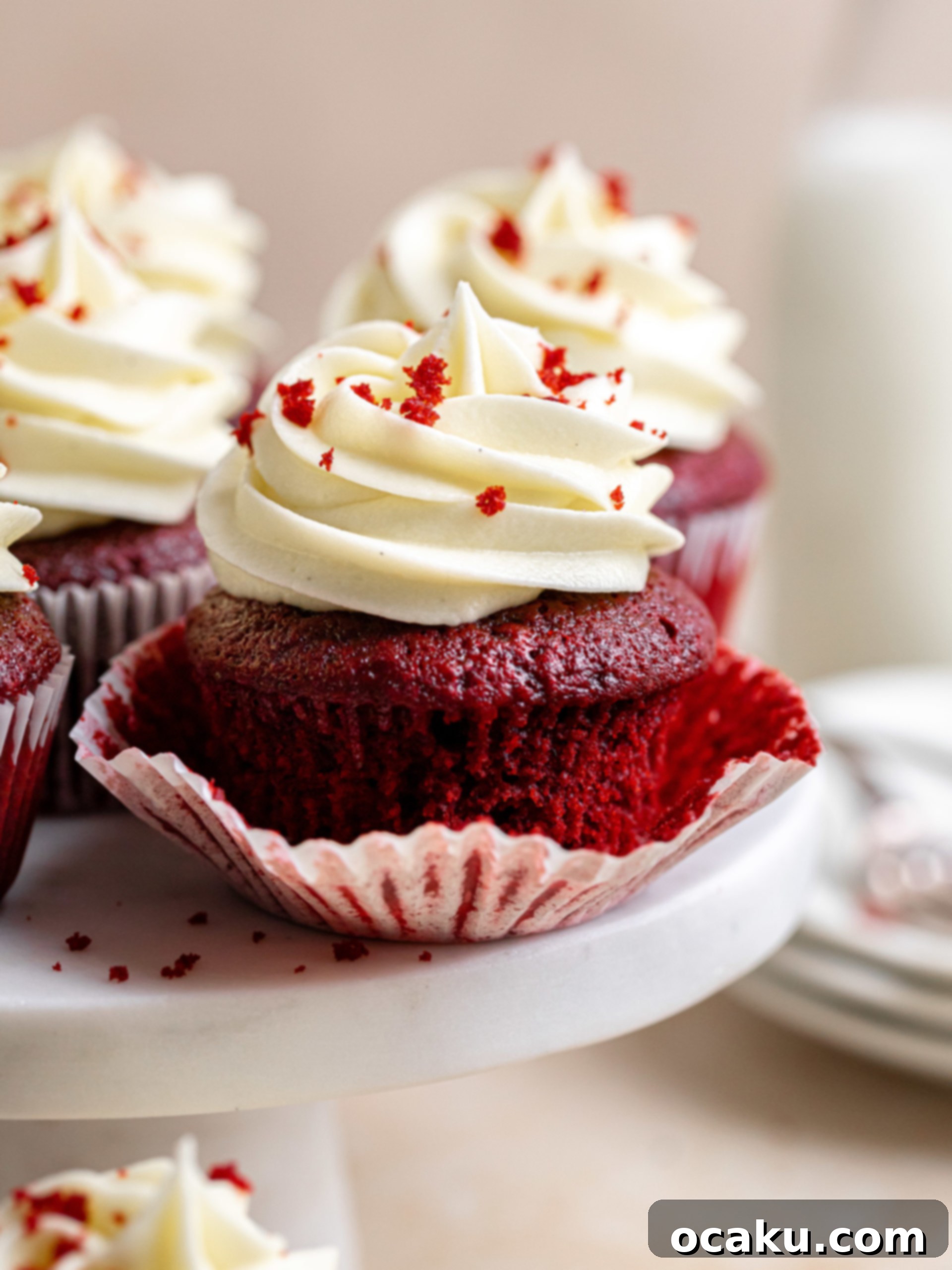 Two perfectly frosted red velvet cupcakes on a rustic white surface