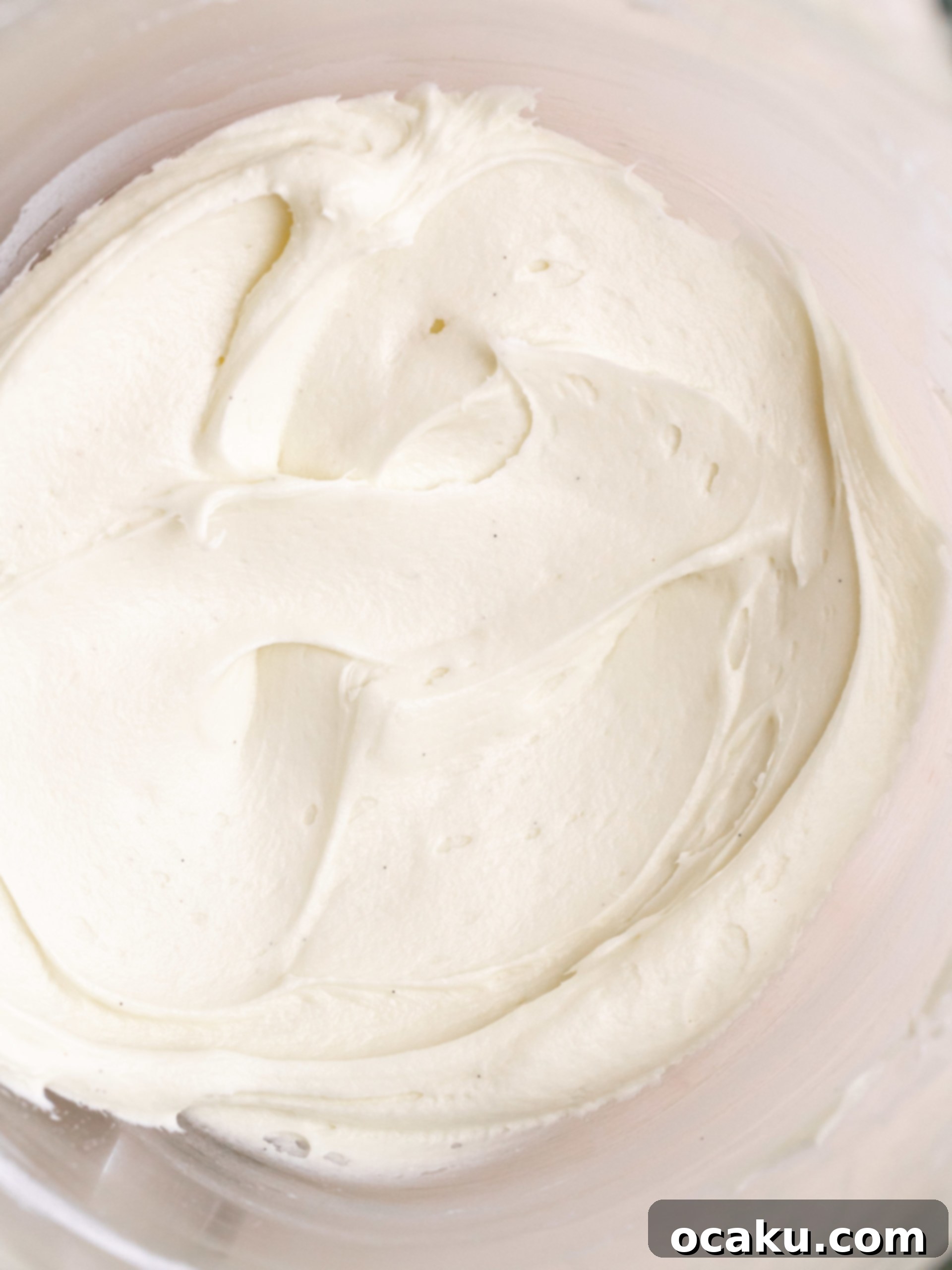 Piping cream cheese frosting onto a red velvet cupcake